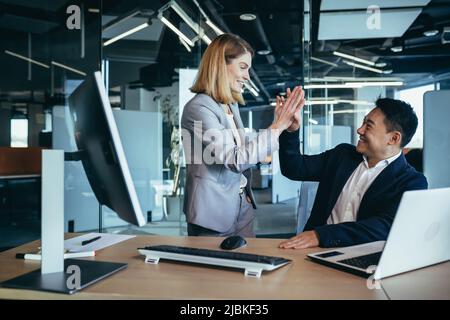 Ein Team von Mitarbeitern, ein Mann und eine Frau Geschäftsleute, arbeiten im Büro, freuen sich über den Erfolg, klatschen zusammen Stockfoto