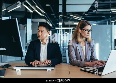 Konzentriertes Team von Geschäftspartnern, die an Computer und Laptop arbeiten, asiatischer Mann und Frau in einem modernen Büro Stockfoto