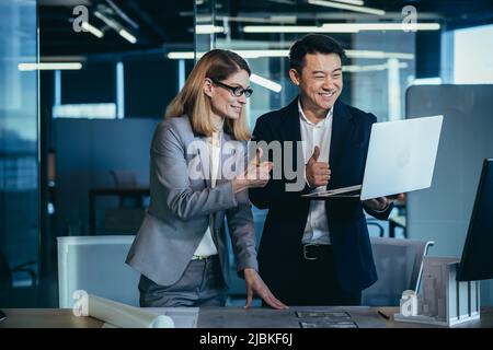 Zwei Architektenteams, die die Kamera betrachten und sich über das abgeschlossene Projekt freuen, halten den Daumen hoch Stockfoto