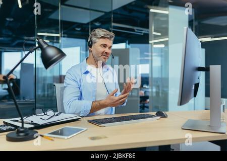 Leitender und erfahrener Mitarbeiter, berät den Käufer bei einem Videoanruf, der Mann arbeitet in einem modernen Büro nutzt Webcam Stockfoto