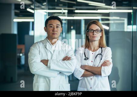 Seriöse und fokussierte Ärzte mit gekreuzten Armen blicken auf die Kamera, asiatische Mann und Frau Team in der Klinik arbeiten Stockfoto