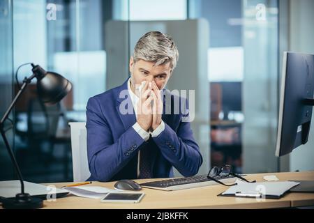 Der Chef-Geschäftsmann arbeitet im Büro, hat eine starke Allergie gegen Niesen und laufende Nase Stockfoto