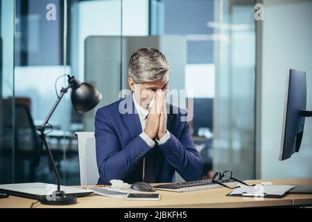 Der Chef-Geschäftsmann arbeitet im Büro, hat eine starke Allergie gegen Niesen und laufende Nase Stockfoto