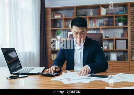 Buchhalter-Wirtschaftsprüfer arbeitet in einem klassischen Büro, berechnet Finanzberichte, asiatische Geschäftsmann arbeitet mit Computer und Dokumenten, Papierkram Stockfoto