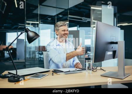 Leitender und erfahrener Mitarbeiter, berät den Käufer bei einem Videoanruf, der Mann arbeitet in einem modernen Büro nutzt Webcam Stockfoto