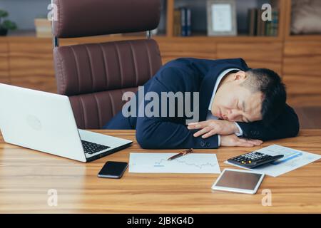 Asiatischer Geschäftsmann schläft müde auf dem Tisch liegend, Mann bei der Arbeit Stockfoto