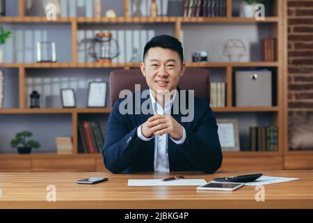 Erfolgreicher asiatischer Makler Geschäftsmann schaut auf die Kamera und lächelt, Mann bei der Arbeit sitzt am Tisch im klassischen Büro Stockfoto