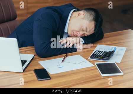 Müde junge asiatische Mann Geschäftsmann, Arbeiter. Der Anwalt schlief bei der Arbeit im Büro auf seinen Händen auf dem Schreibtisch ein Stockfoto