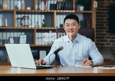 Asiatische Freiberufler nimmt Audio-Podcasts, Geschäftsmann arbeitet im Büro, verwendet professionelles Mikrofon und Laptop Stockfoto