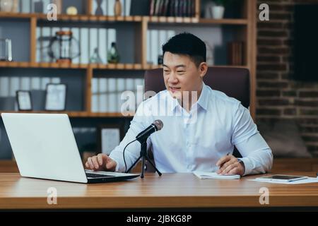 Asiatische Freiberufler nimmt Audio-Podcasts, Geschäftsmann arbeitet im Büro, verwendet professionelles Mikrofon und Laptop Stockfoto