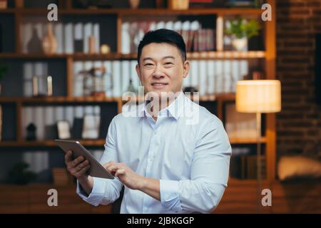 Asiatischer Geschäftsmann, der spät arbeitet, Porträt eines Mannes mit lächelndem Tablet und Blick auf die Kamera Stockfoto