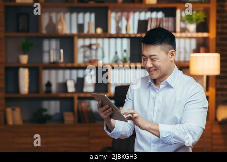 Asiatische Entspannung zu Hause nach der Arbeit, beobachten Online-Video-Kanal auf Tablet, lächeln und jubeln, Geschäftsmann E-Book lesen Stockfoto