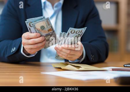 Nahaufnahme der Hände eines Geschäftsmannes, der Bargeld in US-Dollar zählt, und des Mannes, der im Büro arbeitet Stockfoto