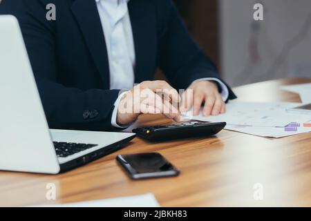 Nahaufnahme der Hände eines Geschäftsmannes, der auf dem Rechner zählt, und des Mannes, der am Tisch arbeitet Stockfoto