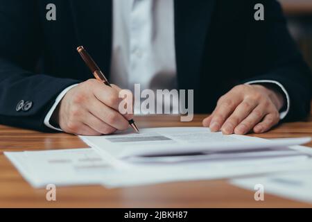 Nahaufnahme der Hände eines asiatischen Geschäftsmannes, der Bankdokumente unterschrieb, eines Mannes, der im modernen Büro arbeitet, am Tisch sitzt, des Bankers Papierkram Stockfoto
