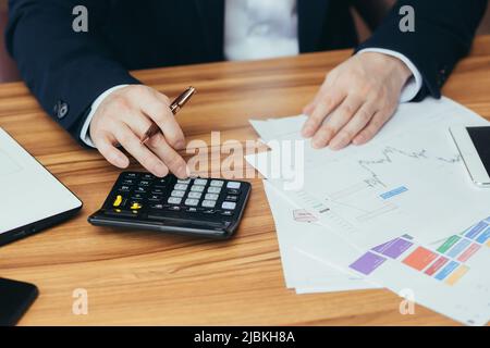 Nahaufnahme Fotohands eines jungen männlichen Buchhalters, Geschäftsmannes, Direktor arbeitet mit Dokumenten, zählt auf einen Rechner, schreibt Rechnungen im Büro des Stockfoto