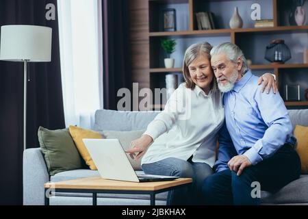 Ältere Paare, Männer und Frauen, die online einkaufen und Laptops zu Hause surfen. Ältere Familie glückliches Rentnerpaar mit Computereinhaken am Bildschirm und bezahlen Stockfoto