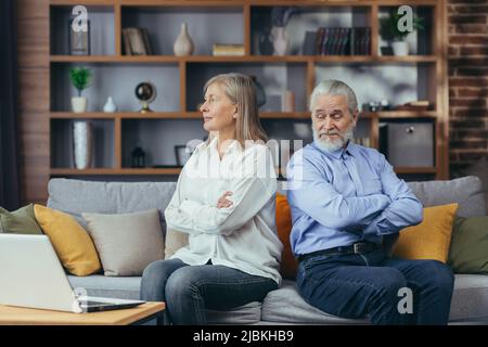 Streitsüchtige Paare, ältere Frauen und Männer, die auf der Couch saßen, beleidigten sich und schauten in verschiedene Richtungen, Familienkonflikte Stockfoto