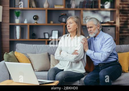 Ein streitsüchteres Paar, ein grauhaariger Mann und eine Frau sitzen auf der Couch und unterhalten sich mit einem Familienpsychologen und nutzen einen Laptop für einen Videoanruf Stockfoto