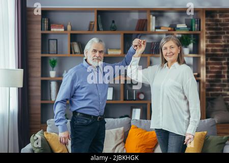 Fröhliche fröhliche ältere verheiratete Paar Spaß zu Hause. Ältere Familie tanzt. Grauhaarige Rentner freuen sich über den aktiven Lebensstil. Alter Mann und wo Stockfoto