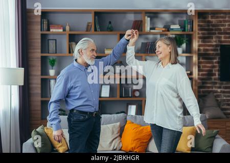 Fröhliche fröhliche ältere verheiratete Paar Spaß zu Hause. Ältere Familie tanzt. Grauhaarige Rentner freuen sich über den aktiven Lebensstil. Alter Mann und wo Stockfoto