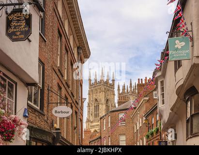 Die oberen Stockwerke einer historischen Straße mit den Türmen des York Minster in der Ferne. Die Union Flags fliegen über die Straße und ein wolkiger Himmel i Stockfoto