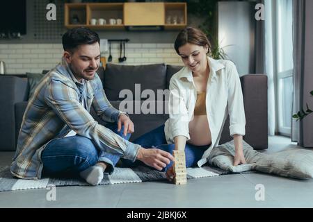 Junges Paar, Mann und Schwangere, spielen Brettspiel von jang zusammen, sitzen auf dem Boden zu Hause, Spaß zusammen Stockfoto