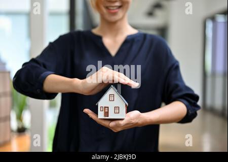 Zugeschnittenes Bild, eine Maklerin oder Maklerin einer Hausversicherung, die ein Hausmodell im Büro hält. Hausversicherung Geschäftskonzept. Stockfoto
