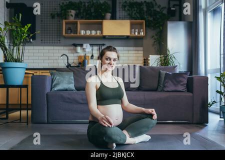 Eine Schwangerin meditiert und praktiziert Yoga in einer Lotusposition zu Hause Stockfoto
