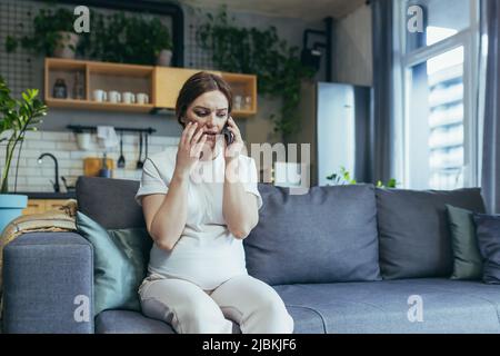 Traurige, schwanger Frau zu Hause ängstlich am Telefon auf der Couch sitzend Stockfoto