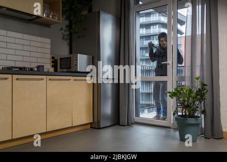 Männlicher Dieb in schwarzen Kleidern, der versucht, das Türschloss im Haus zu brechen Stockfoto