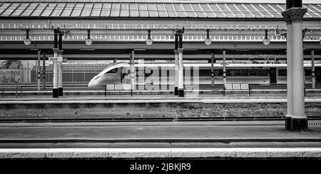 Ein eleganter, langgestreckter, moderner Zug ruht auf einem Bahnhofsplatz. Ein historisches Vordach mit Säulen ist oben und ein Besatzungsmitglied steht an einer Tür. Stockfoto