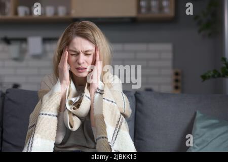 Die kranke Frau sitzt zu Hause auf der Couch, hat Husten und Fieber, kalte und laufende Nase Stockfoto