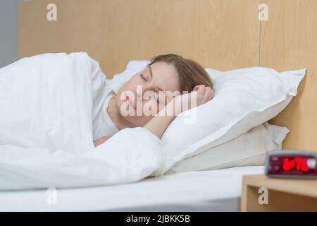 Nahaufnahme einer Frau, die unter einer Decke schläft und in einem Traum lächelt Stockfoto