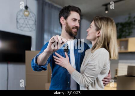 Ausgewählte Fokus, verheiratetes Paar Mann und Frau glücklich zusammen, umarmt, die Schlüssel zu ihrer neuen Wohnung, Hausarmung, Nahaufnahme Stockfoto
