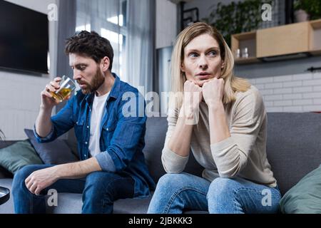 Junge Familie fällt auseinander, deprimierte Frau wegen des alkoholischen Ehemanns, Paar sitzt auf dem Sofa im Wohnzimmer Stockfoto