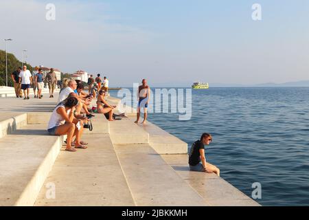 ZADAR, KROATIEN - 14. SEPTEMBER 2016: Das sind nicht identifizierte Urlauber auf den Stufen der Stadtpromenade bei Sonnenuntergang. Stockfoto