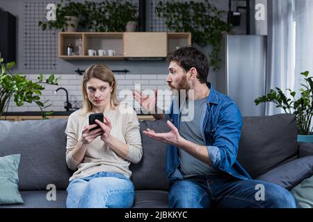 Eifersüchtiger Mann, der die Frau am Telefon anschrie, ein Ehepaar, das zu Hause auf dem Sofa saß, streite Stockfoto