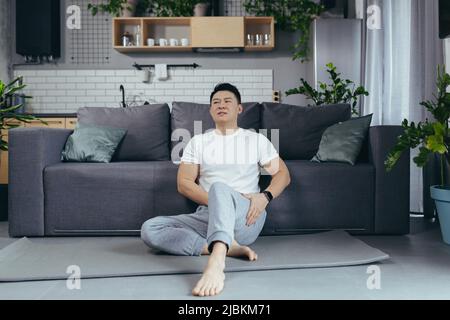 Asiatischer Mann in Sportkleidung, der zu Hause an Knieschmerzen leidet Stockfoto