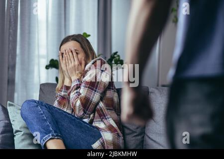 Häusliche Gewalt, wütender Mann, der Frau schrie und schlug, Nahaufnahme, weinende Frau, die auf dem Sofa saß Stockfoto