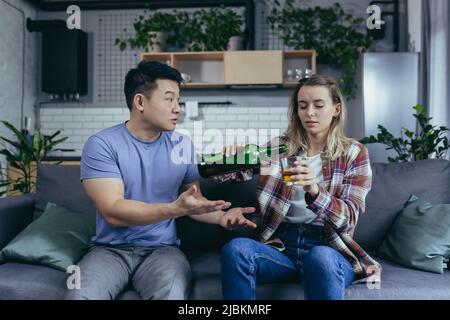 Alkoholikerin, die zu Hause harten Alkohol trinkt, Ehemann frustriert und verärgert, Konflikt in der jungen Familie um Alkohol Stockfoto