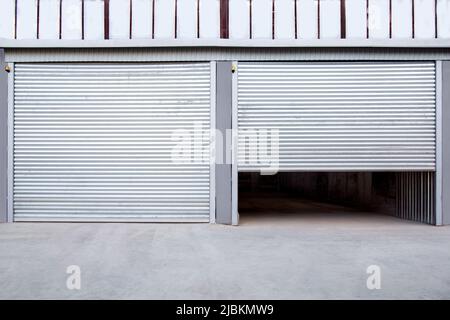 2 Graue Eisentür? Von Garage und Industriegebäude Lagerhaus Außenfassade mit grauer Betonstraße, Vorderansicht auf schließendes Tor niemand. Stockfoto