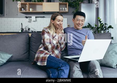 Glücklich jung asiatisch paar bonding lachend mit Laptop sitzen am Tisch zu Hause Stockfoto