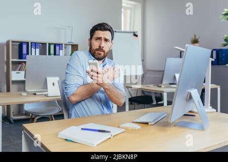 Der Geschäftsmann arbeitet tagsüber in einem modernen, hellen Büro, ein Mann hält kalt eine Fernbedienung von der Klimaanlage, erhöht die Temperatur Stockfoto