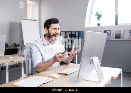 Trauriger und ängstlicher Mann, der im Büro arbeitet, Geschäftsmann, frustriert durch das Ergebnis der Arbeit, müde und niedergeschlagen, wenn er auf den Bildschirm schaut Stockfoto