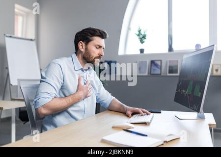 Kranker Geschäftsmann, der im Büro arbeitete, machte sich Sorgen und hielt seine Hand an seine Brust, schwere Herzschmerzen Stockfoto