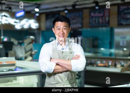 Porträt eines asiatischen Verkäufers im Fisch- und Fischgeschäft, lächelnd mit gekreuzten Armen und mit Blick auf die Kamera Stockfoto