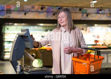 Lächelnde ältere Frau wiegt Gemüse im Supermarkt Stockfoto