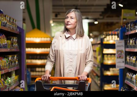 Ein grauhaariger Rentner in einem Lebensmittelgeschäft wählt Lebensmittel Stockfoto