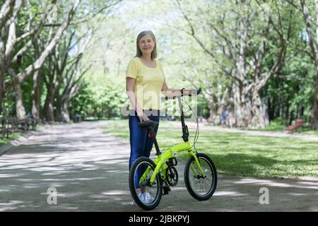 Eine pensionierte Frau, die sich im Park ausruhte, eine grauhaarige Perserin, die an einem Sommertag mit einem Fahrrad unterwegs ist Stockfoto